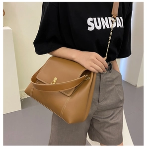 Close-up of brown leather crossbody bag with golden twist lock and chain strap