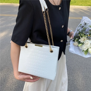 White croc-effect tote bag with gold chain handles carried by a model in nature