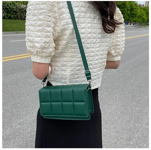 Detail of dark green quilted crossbody bag featuring adjustable leather shoulder strap