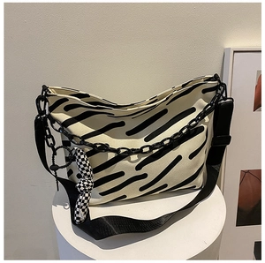 Detail of canvas tote bag featuring black stripes, chunky chain and checkerboard charm