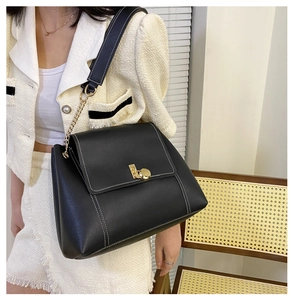 Close-up of black leather crossbody bag featuring white contrast stitching and gold clasp