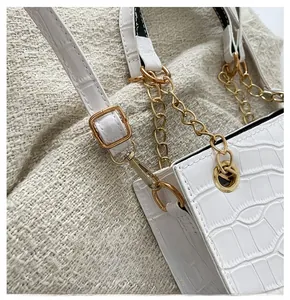 Detail of white crocodile texture leather bag with golden metal hook and chain strap