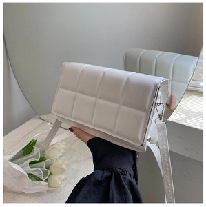 Detail of white quilted crossbody bag with jagged stitching and silver metal hooks