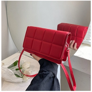Detail of red quilted square shoulder bag with padded lattice texture and slim strap