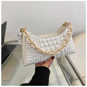 Detail of white quilted handbag with chunky gold and resin chain on a modern desk