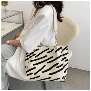 Detail of canvas tote bag featuring black stripes and silver chain link on shoulder strap