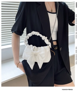 Détail du sac à main blanc à nœud avec poignée froncée et chaîne sur un costume noir