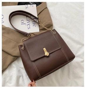 Detail of dark brown leather crossbody bag with white stitching and gold turn-lock closure