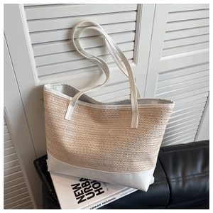 Close-up of beige straw tote bag with white leather trim on a black leather sofa
