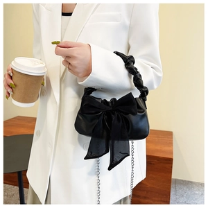 Détail d'un sac à main noir chic avec nœud en maille, chaîne et poignée plissée