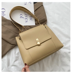 Detail of beige leather crossbody bag featuring a gold round lock and metal chain strap