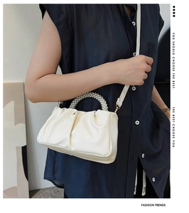 Detail of white pleated cloud bag featuring elegant pearl handle and slim crossbody strap
