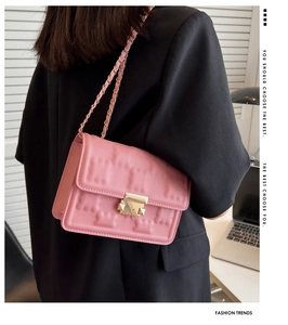 Detail view of pink quilted shoulder bag featuring gold lock and leather chain strap