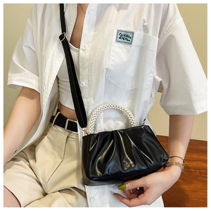 Detail of black pleated cloud bag with pearl handle and leather strap on model