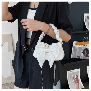 Gros plan d'un sac à main blanc plissé avec un grand nœud décoratif et une bandoulière chaîne