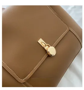 Close-up of golden circular buckle on brown leather crossbody bag with white stitching