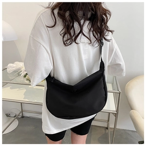 Rear view of a minimalist black crescent nylon crossbody bag on a model with a wide strap