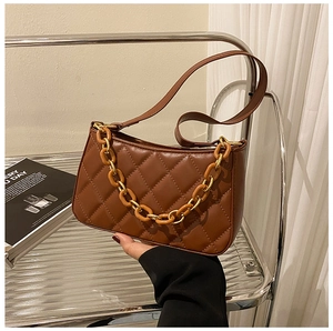 Gros plan sur le cuir matelassé marron et les détails de la chaîne de ce sac porté épaule