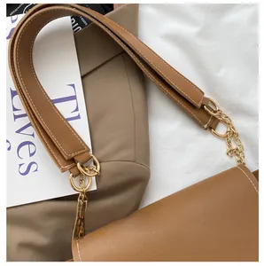 Close-up of brown leather bag featuring wide strap and golden metal chain link details