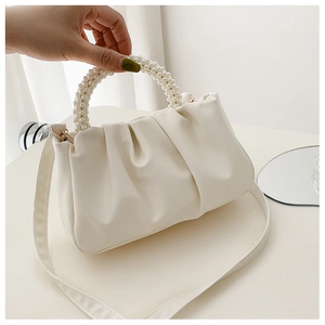 Detail of cream white pleated cloud bag featuring decorative pearl bead handle and PU leather