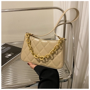 Détail macro du sac beige matelassé avec une grosse chaîne décorative jaune tendance