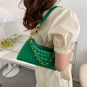 Bright green quilted baguette bag with thick gold chain on model in chic indoor setting