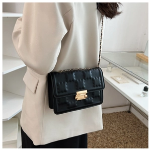 Detail of black crossbody bag featuring gold chain strap and quilted pattern texture