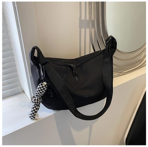 Detailed view of black nylon crossbody bag with checkerboard plush charm and adjustable strap