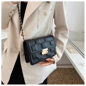 Detailed view of black quilted crossbody bag with gold chain strap on beige blazer