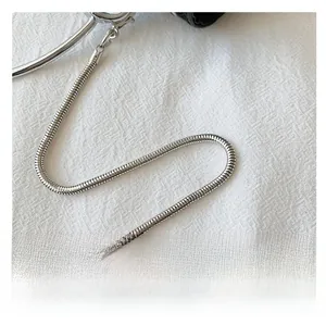 Detail of silver snake chain strap with polished metal clasp on textured white fabric