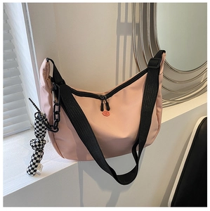 Pink nylon crossbody bag with black chain detail and checkered charm on a window sill
