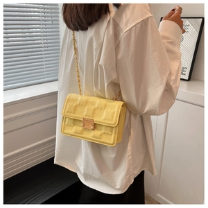 Detail of lemon yellow crossbody bag with brick texture and golden chain strap on model