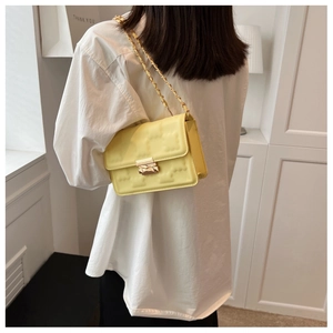 Detail of yellow quilted chain shoulder bag worn by model in a minimalist bright setting
