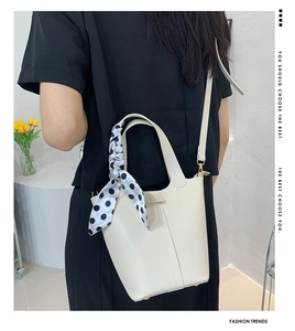 Detail of a creamy white bucket bag featuring a polka dot silk scarf and thin strap