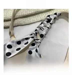 Detail of cream leather bucket bag handle wrapped with a black polka dot silk scarf