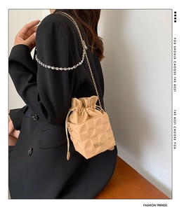 Quilted beige bucket bag with gold chain strap shown on a model's shoulder