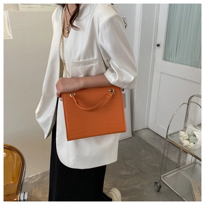 Détail du sac orange texturé croco avec chaîne dorée sur une veste de costume blanche