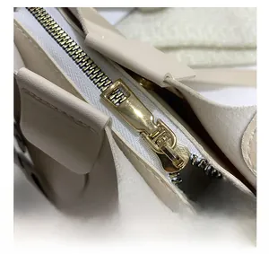 Close-up of golden metal zipper and stitching detail on beige leather handbag