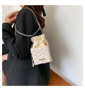 Detail of cream white quilted bucket bag featuring a gold chain strap and metal logo plate