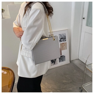 Détail du sac bandoulière gris effet crocodile avec chaîne dorée sur costume blanc