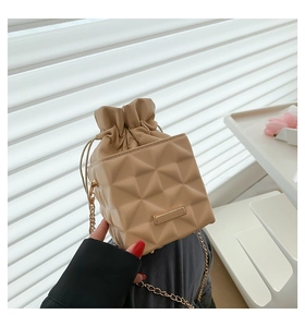 Detail of beige bucket bag with chain strap and textured diamond quilted geometric pattern