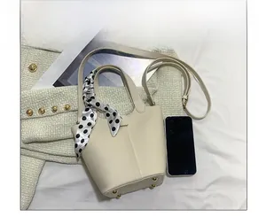 Close-up of beige leather bucket bag with polka dot scarf handle and golden base feet