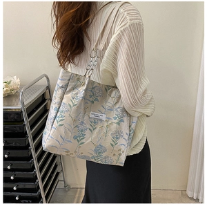 Detail of floral tote bag showing chain strap and logo patch on off-white fabric
