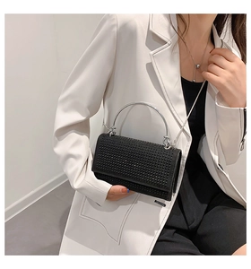 Detail of a black rhinestone square clutch bag with silver metal handle on a white blazer
