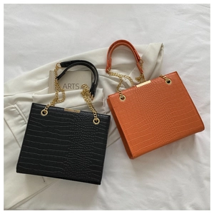 Détail de sacs cabas à motif crocodile noir et orange avec anses en chaîne dorée