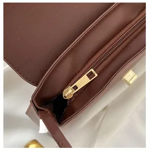 Detail view of smooth golden zipper and internal pocket on a dark brown leather handbag