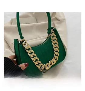 Detail shot of green crocodile pattern baguette bag featuring thick gold chain strap