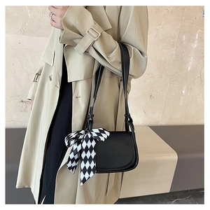 Detail of black crossbody bag featuring a chic checkered scarf decoration on shoulder strap