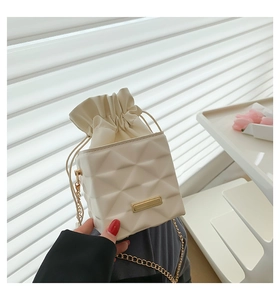 Detailed view of cream quilted bucket bag featuring golden chain and metallic nameplate