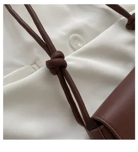 Detail of knotted leather shoulder strap and fine stitching on a brown minimalist handbag